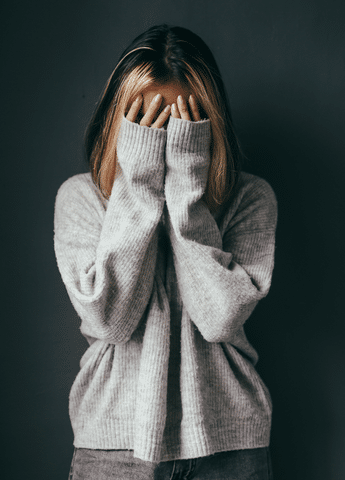 Girl wearing white sweater crying and covering her face with her hands