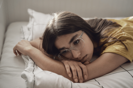 Young girl wearing glasses laying on her bed