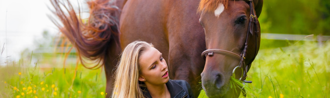Blond girl with a horse in a grass field